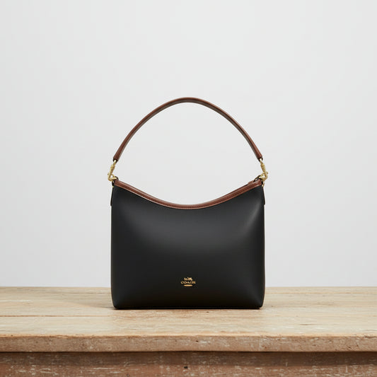Black handbag with brown handle on a wooden table in an indoor setting